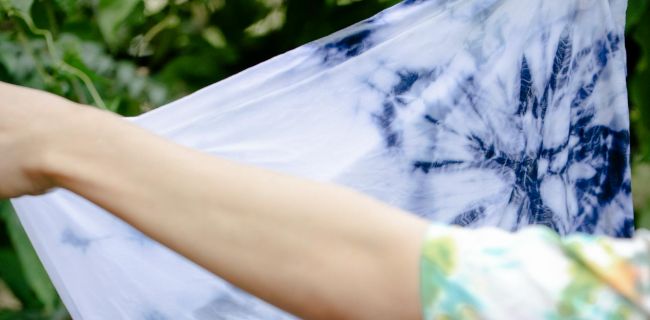 Arme halten ein nasses weißes T-shirt mit blauem Batik-Muster hoch
