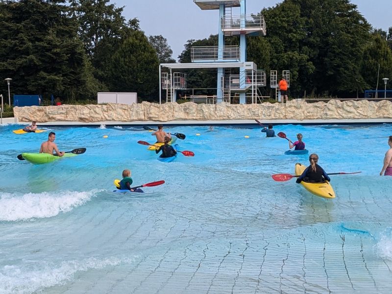 Kinder paddeln im Kajak im Wellenbecken des Freibads