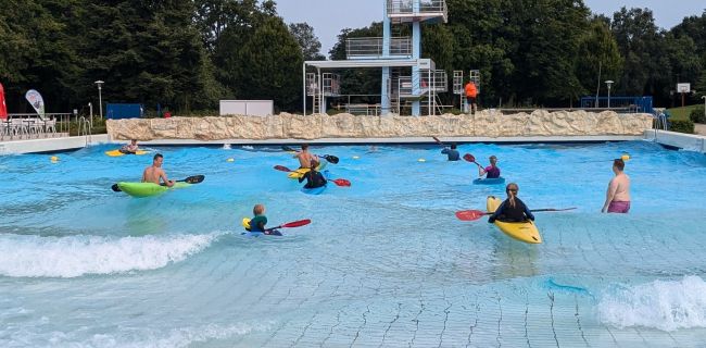 Kinder paddeln im Kajak im Wellenbecken des Freibads